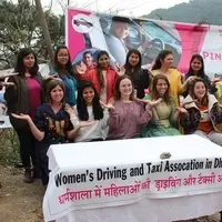 A group of smiling women around a table with a banner reading Women's Driving and Taxi Association in Dharamshala.