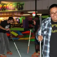 Three students holding white canes roller skate. One in front smiles, while the two in back skate towards each other.