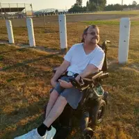Mark is giving a thumbs-up signal as he sits in a park.