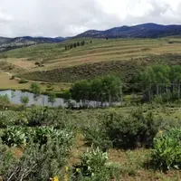 Four people stand shoulder to shoulder along a grassy ridge-line overlooking fields and a small lake in Eastern Washington.