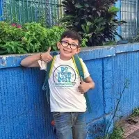 happy latino boy smiling standing outside with his backpack on giving a thumbs up, wearing a Do your Best Outreach360 Virtual English Academy t-shirt