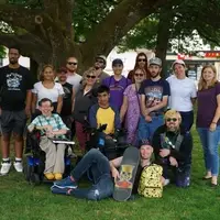 A group of CFI participants and staff with various visible and invisible disabilities smile for the camera in a park.