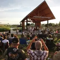 A crowd sits in a grassy park looking towards an outdoor stage, where a band is playing at dusk.