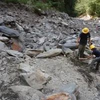 Two people conduct trail improvements in a rocky section of a trail.