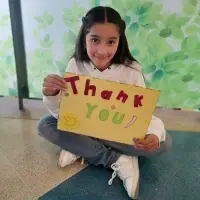 young Colombian girl holding thank you sign smiling sitting on floor