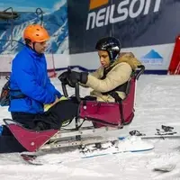To make skiing accessible, Hazel uses a sit ski. James supports her by holding on to the back of the seat and steering.