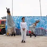 Performers with full-body puppets, performing in front of a painted bus