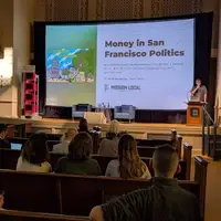 A speaker stands at a lectern in front of a large projection screen that has a slide with the text Money in San Francisco politics.