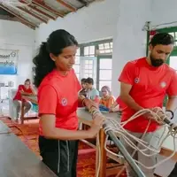 Volunteers in red T-shirts work with ropes and a pole while others watch.