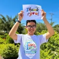 latino youth male smiling standing outside in sun wearing an Outreach360 t-shirt and holding up a Thank you sign