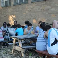 People of many ages and races sitting at outdoor picnic tables enjoying an evening meal