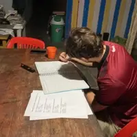 An NGO management intern at Semillas Life organizing administrative documents and planning monthly community activities in Codo del Pozuzo, Peru. The intern is working on paper-based tasks to coordinate local conservation and education projects in the Amazon