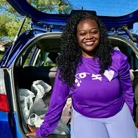 Smiling woman in purple shirt in front of a trunk filled with grocery bags