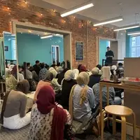 Muslims gathered in a room, sitting on the floor, listening to a Friday sermon