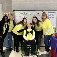 Staff standing around a young man with cerebral palsy who uses a wheelchair for mobility.