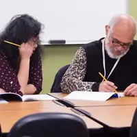 A man writes in a workbook while a tutor gives support, in the Literacy Center