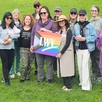 LWVSF members take a group photo in a park. They hold a sign that has the League logo and the pride flag.