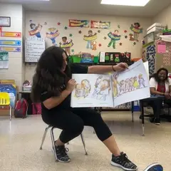 A woman reading a picture book to a class.