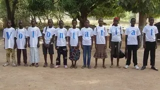 Children stand in a row, each wearing a shirt with a different letter.