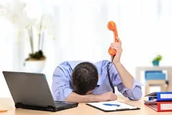 A man, fed up, with his head on the table and holding a telephone.