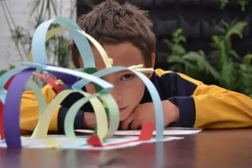 Foto de niño mirando a la cámara a través de una manualidad con papeles