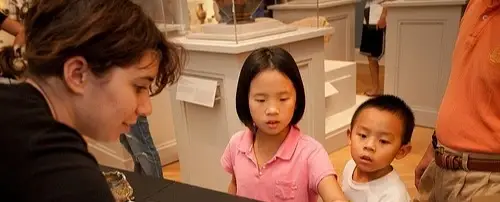 A woman shows two children something at a table.