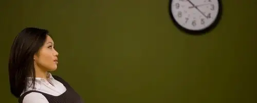 A woman sitting and thinking. A clock is on the wall.