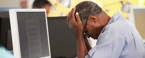 A person at their work desk. They have their head in their hands.