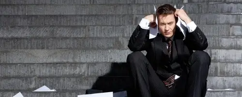 A man in a suit covers his ears with work papers.