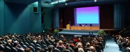 A crowded conference room with people sitting in chairs.