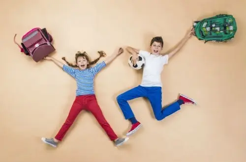Foto de niño y niña escolares saltando con una mochila en mano