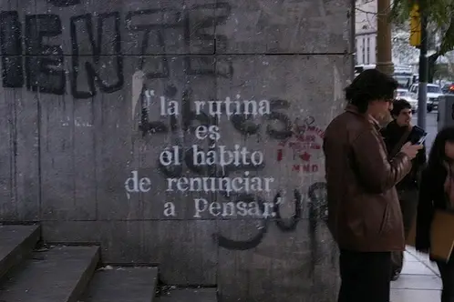 A person looking at his phone and standing a wall.