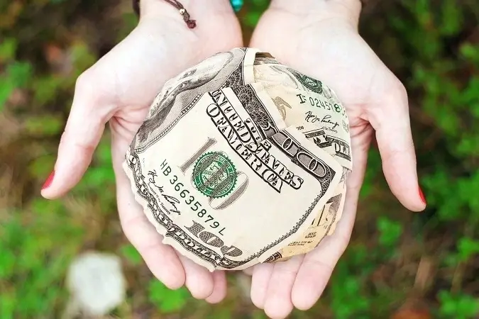 Dos manos sosteniendo una bola con billetes