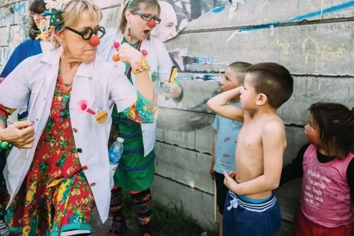 Women in lab coats dressed as clowns flexing comically for children.