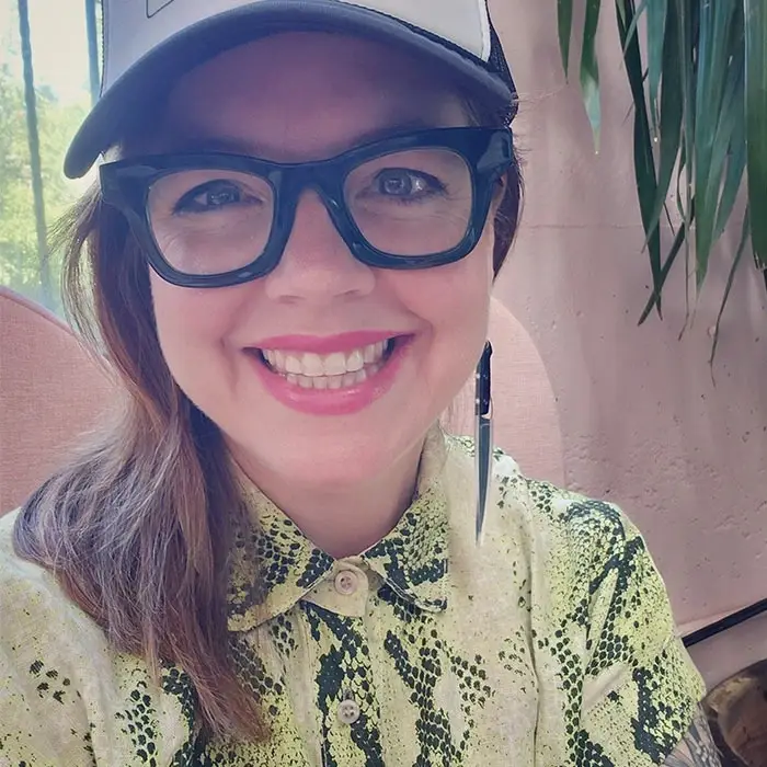A woman wearing a cap and black glasses smiling