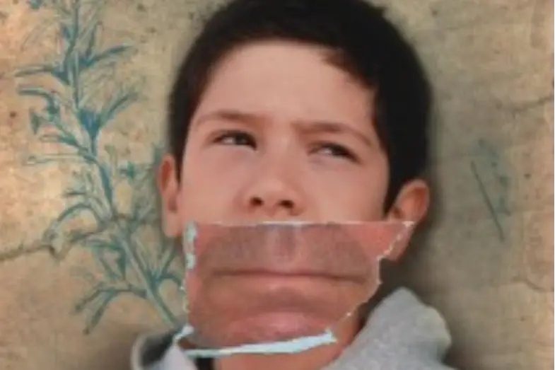 A young boy stares pensively with a photo of a man's mouth over his own.