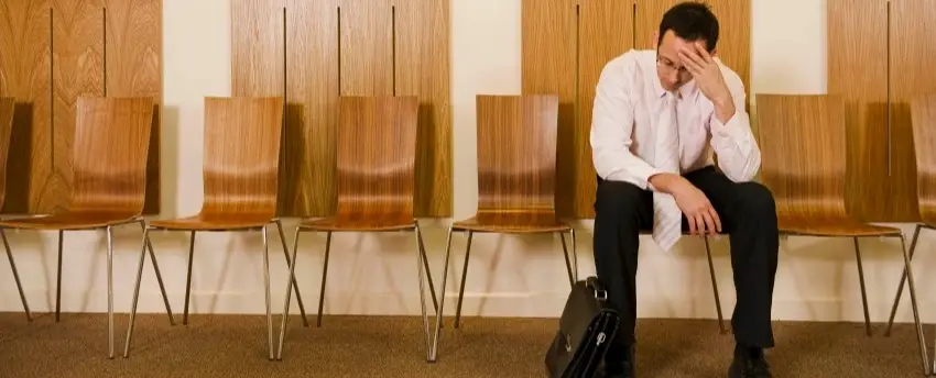 A lone man sitting in a row of chairs with his head in his hand.
