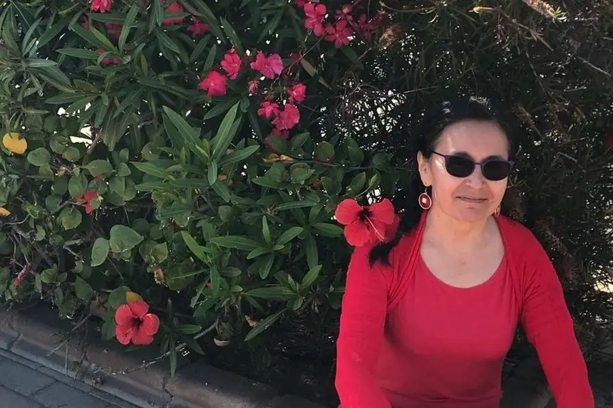 Foto de Luz María Rodríguez sonriendo sentada junto a unos arbustos con flores