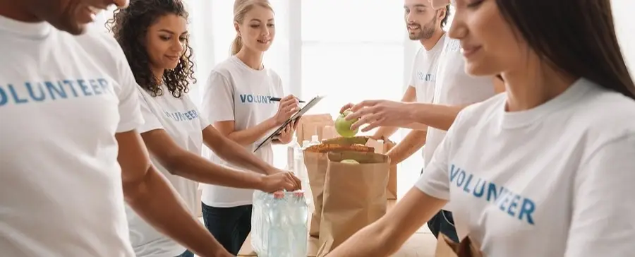 A group of volunteers packing food into paper bags.