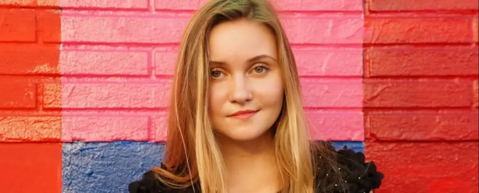 A woman smiles in front of a colorful brick wall.
