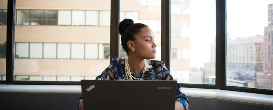 A person with a laptop looking out a window.
