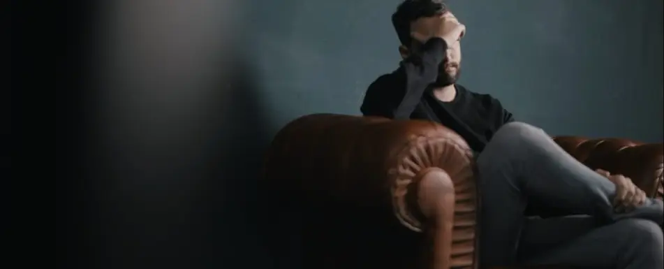 A man on a couch with his hand covering his face.