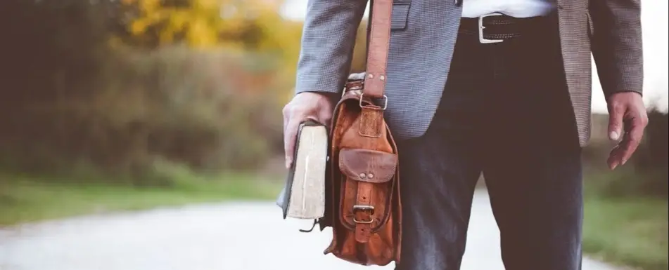 Someone in a suite wearing a satchel and holding a book.