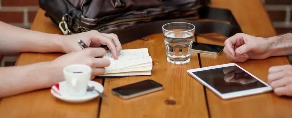 Two people sit at a table with objects between them.