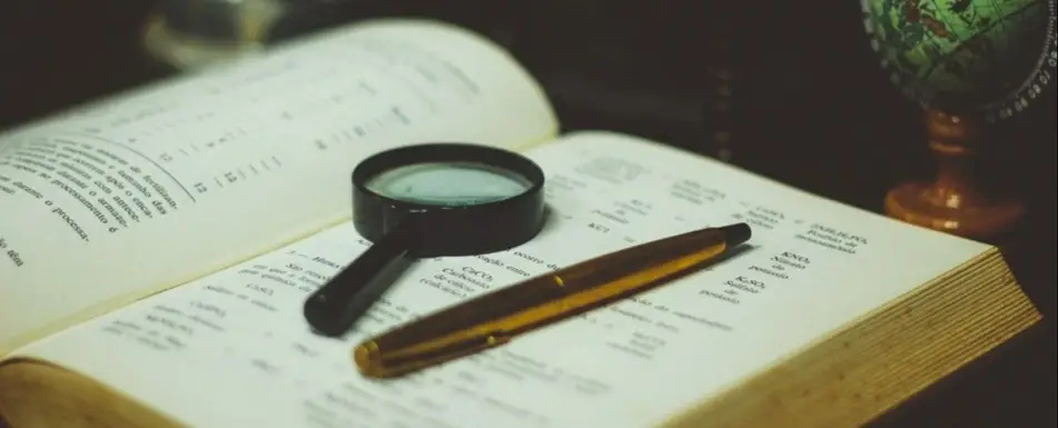 A book with a magnifying glass and a pen on it.