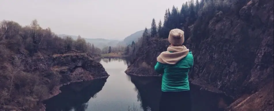 A woman looks out at a tree lined river.