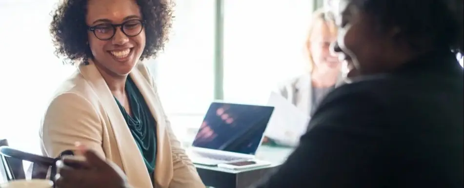 A bespectacled woman laughing in a meeting.