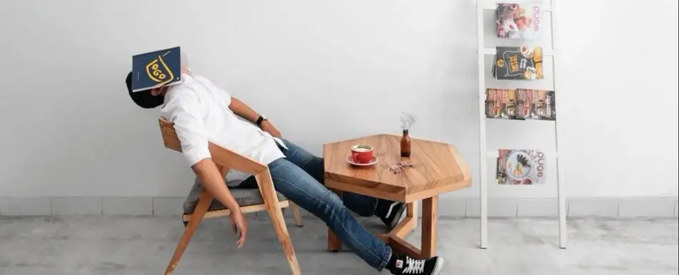 Someone sleeping on a chair. He has an open book on his face.