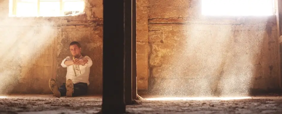 A man sitting by a wall holding an empty bottle.