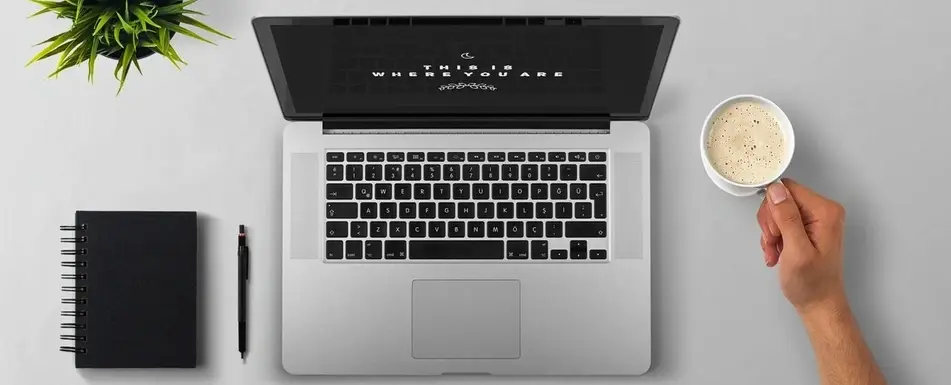 A work desk with a cup of coffee, a laptop and a notebook.